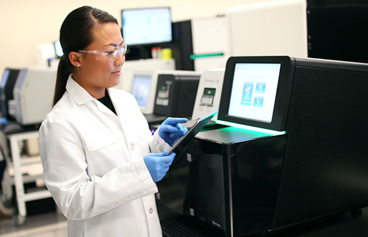 Person wearing blue gloves pointing to a paper next to a sequencer